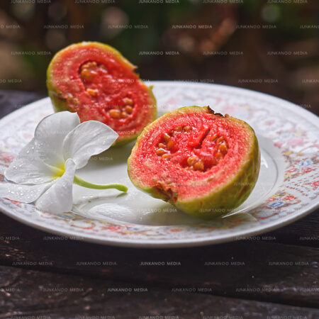 Two Bahamian guava slices on a saucer with a white flower.
