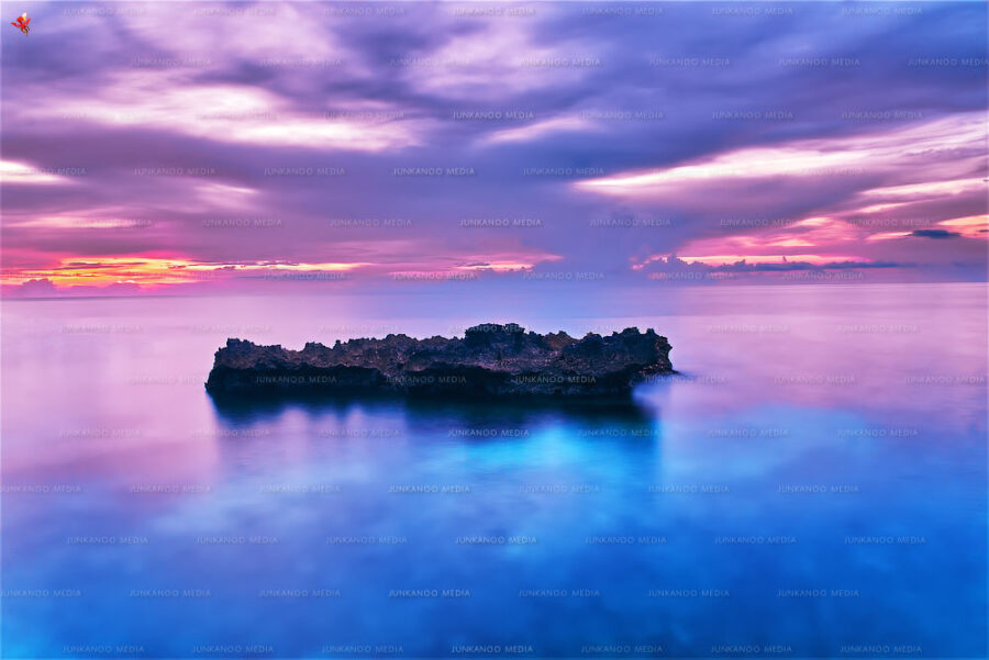 A long exposure of a rock formation sitting in the ocean.