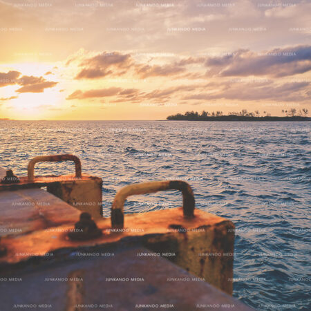 Sunset at Arawak Cay with ladder in foreground and island in the background under low lying clouds.