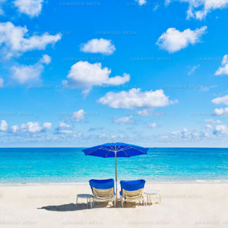 Two chairs on the beach under a blue sky with white puffy clouds.