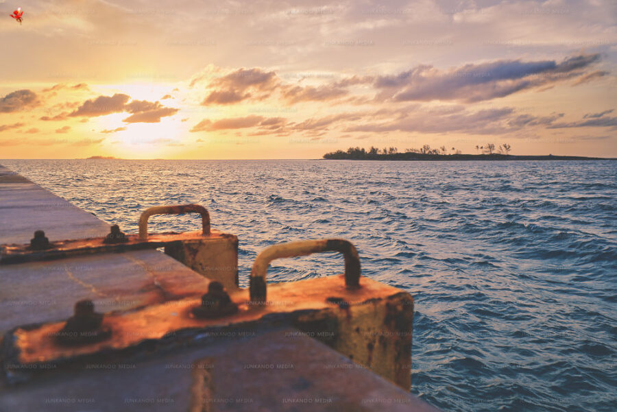 Sunset at Arawak Cay with ladder in foreground and island in the background under low lying clouds.