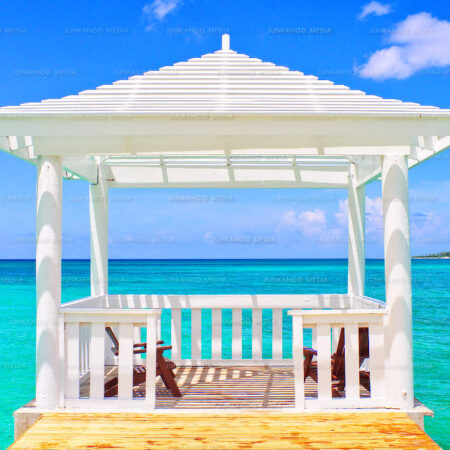 A gazebo in the middle of a turquoise ocean with an island in the background.