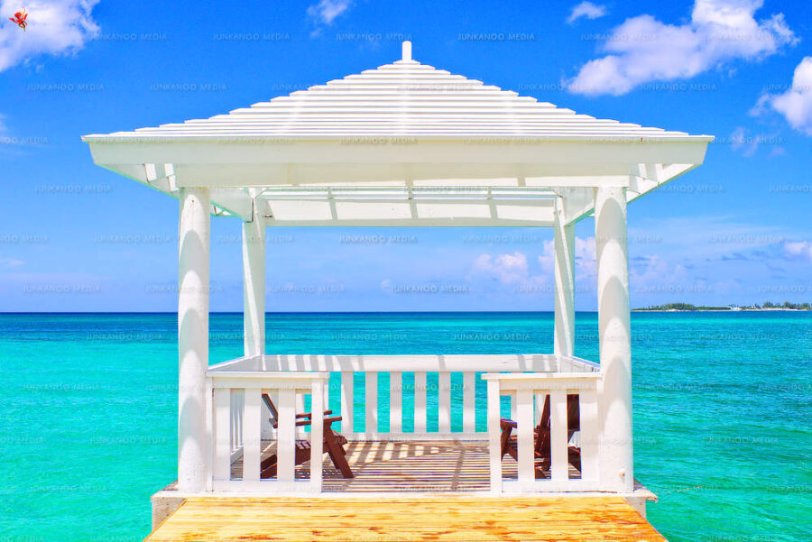 A gazebo in the middle of a turquoise ocean with an island in the background.