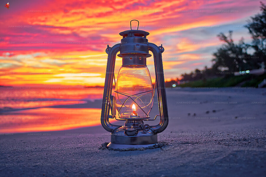 Lantern on Cabbage Beach sitting on sand with ocean and morning sunrise in background.