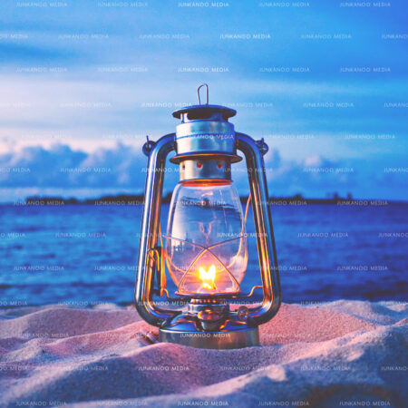 A paraffin oil lamp resting on sand with a blue ocean background in the evening in The Bahamas