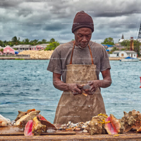A fisherman processes conch with West Bay Street in the background in Nassau Bahamas.