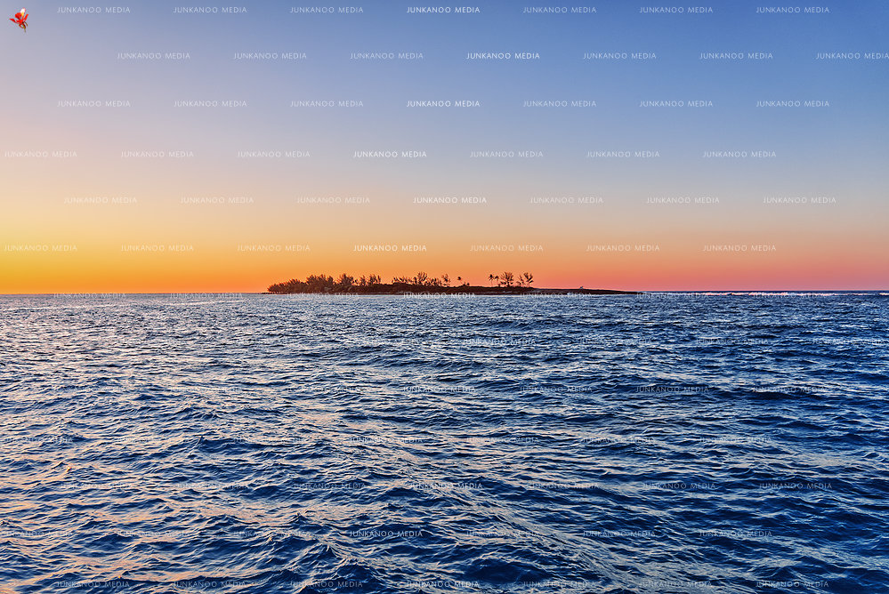 An island sits in the soft glow of sunset surrounded by ocean waves.