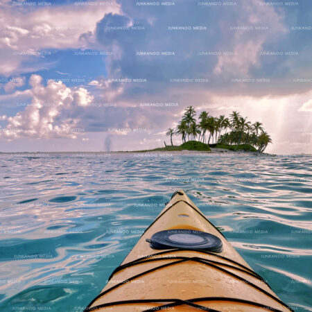 A kayak approaches a small island in The Bahamas with dramatic cloud formations in the background.
