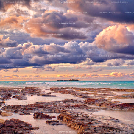 Photo of tidal pools in the foreground with Balmoral Island in the background, underneath immense dramatic cloud cover in The Bahamas.
