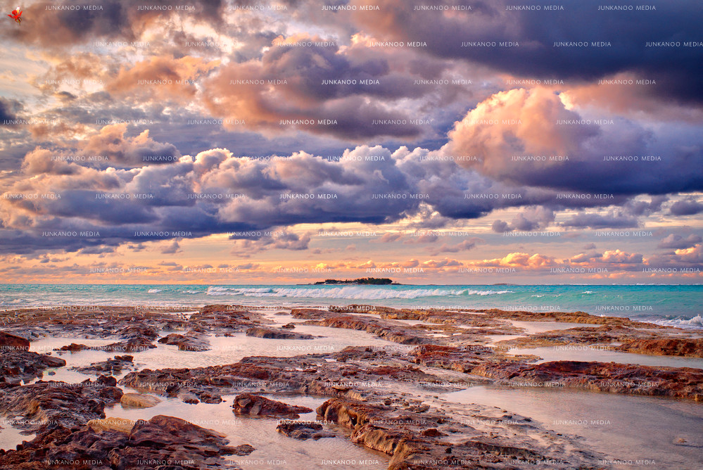 Photo of tidal pools in the foreground with Balmoral Island in the background, underneath immense dramatic cloud cover in The Bahamas.